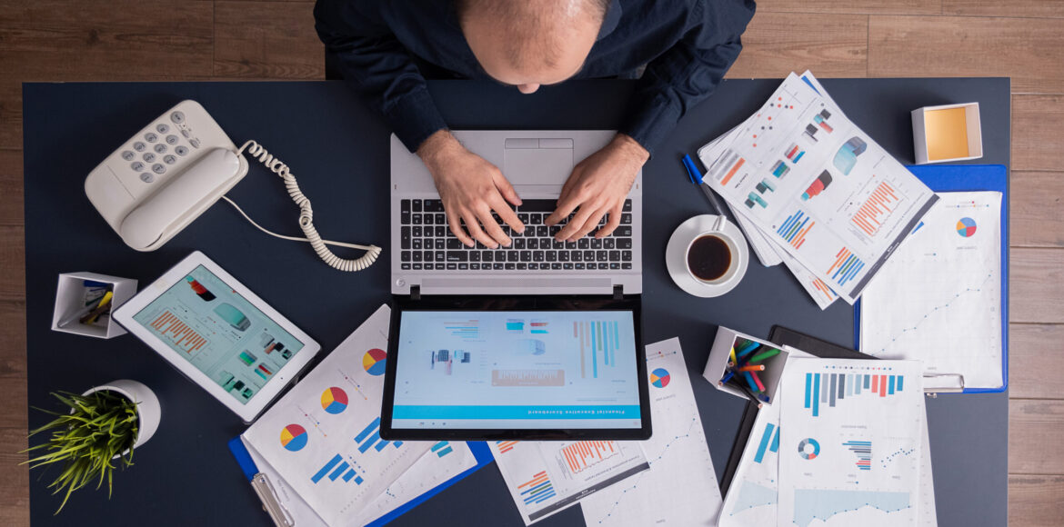 Top view of business man in corporate office sitting at desk Top view of business man in corporate office sitting at desk, typing on laptop, working on financial statistics and business strategy. Entrepreneur using touchepad scrolling through documents.